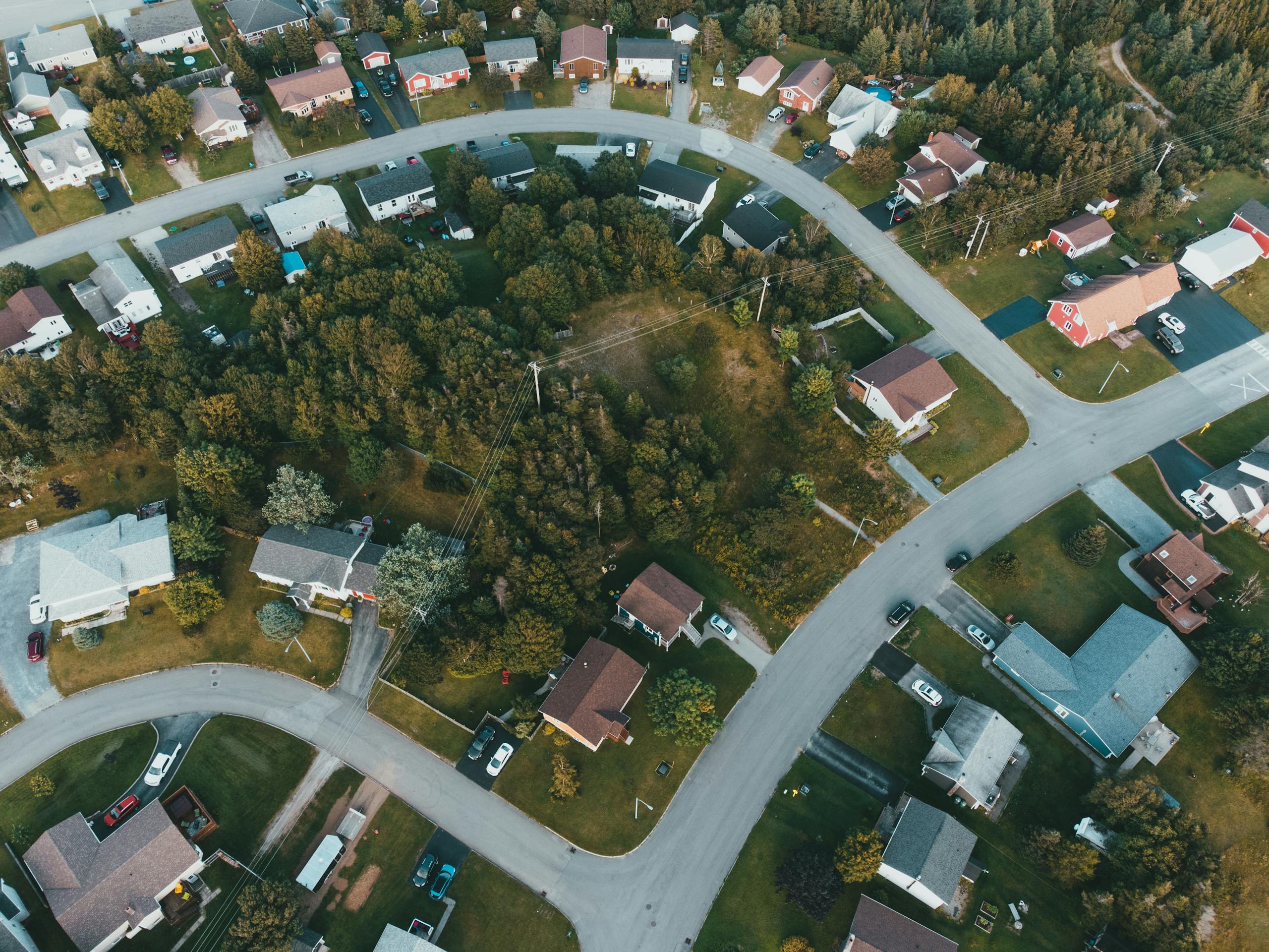 Aerial shot of a suburban neighborhood with houses and lush greenery, captured during the day.